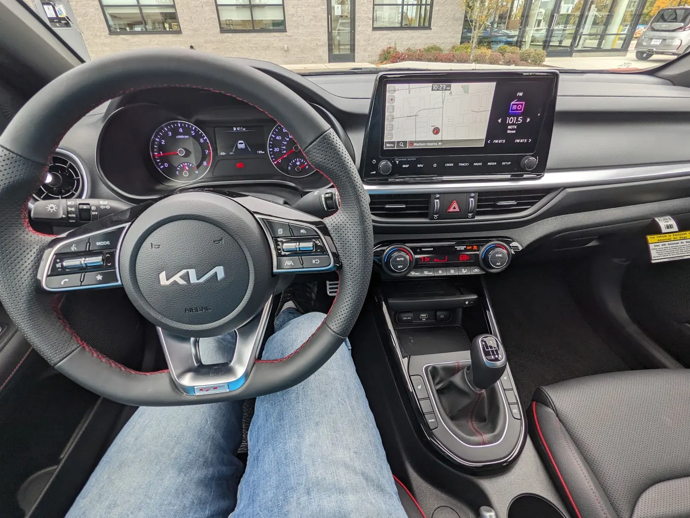 Driver’s view of a Kia Forte GT interior showing the steering wheel, instrument cluster reading 411 miles, and a six-speed manual shifter.