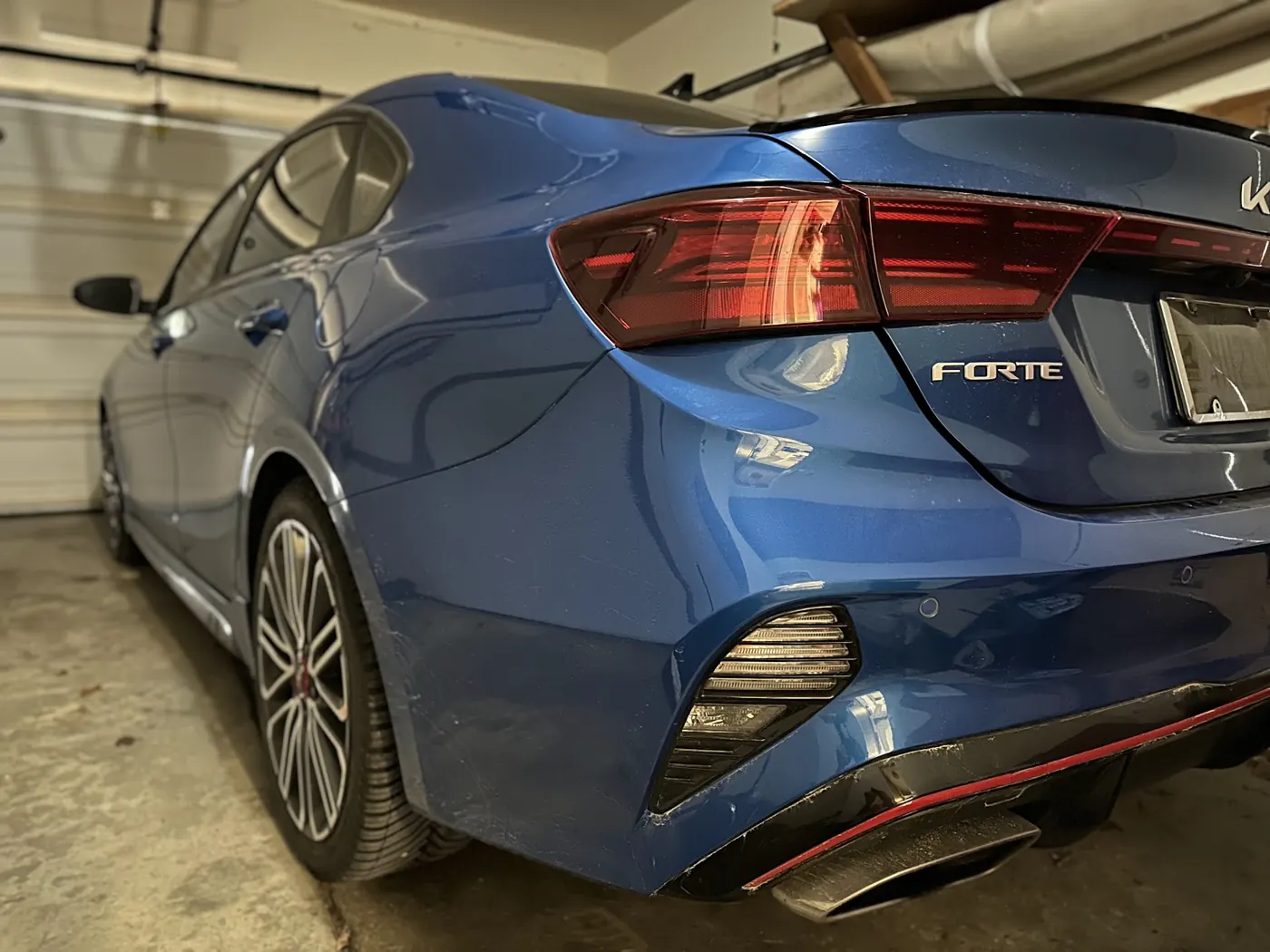 Rear three-quarter view of a blue Kia Forte GT sedan parked in a home garage.